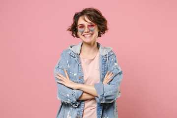 Cheerful young brunette woman girl in casual denim jacket, eyeglasses posing isolated on pastel pink background studio portrait. People lifestyle concept. Mock up copy space. Holding hands crossed.