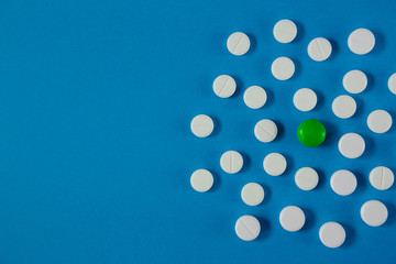 many white pills and one green on a blue background