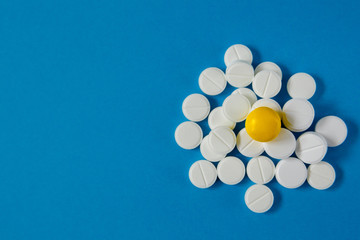 heap of white pills and one yellow, on a blue background