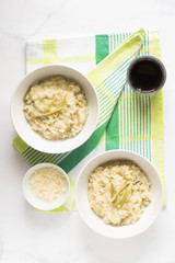 Asparagus risotto in two bowl. A small bowl full of parmesan cheese. A glass full of red wine. Green kitchen towel. White background. 