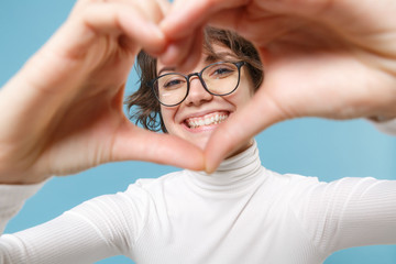 Smiling young brunette woman girl in casual white clothes, eyeglasses isolated on pastel blue background. People lifestyle concept. Mock up copy space. Showing shape heart with hands heart-shape sign.