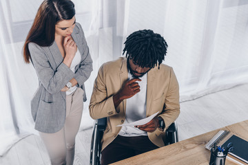 Fototapeta premium High angle view of thoughtful employee near african american disabled recruiter with papers in office