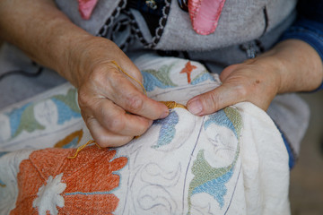 Woman embroiders suzani close up. A type of embroidered and decorative tribal textile made in Uzbekistan