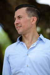 Face of happy young businessman thinking at the park