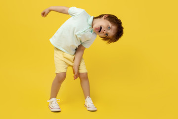 Adorable funny kid listening music and dance over yellow background.
