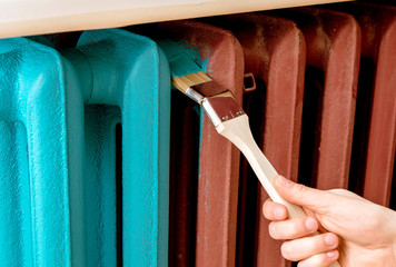 Home refreshing renovation concept. Close up view of man hand painting with special curved radiator...