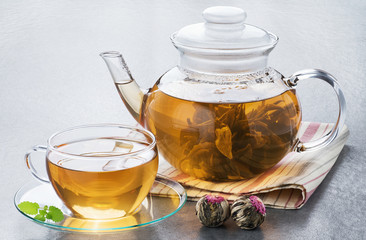 Bound tea in a transparent teapot and a cup of tea on a gray background.