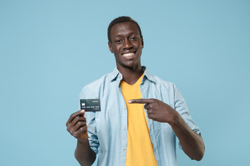 Smiling young african american man guy in casual shirt, yellow t-shirt posing isolated on blue wall...