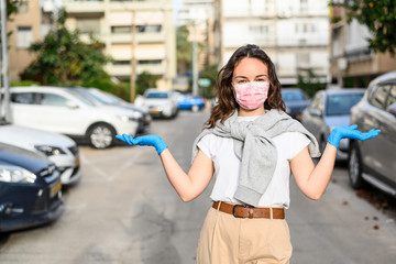 Brunette girl in a disposable mask and protective gloves spreads her arms to the sides, stands on the street. The concept of self-defense and prevention of viruses, epidemics. Urban. Close-up.