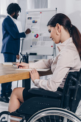 African american recruiter near flip chart and disabled employee writing in notebook