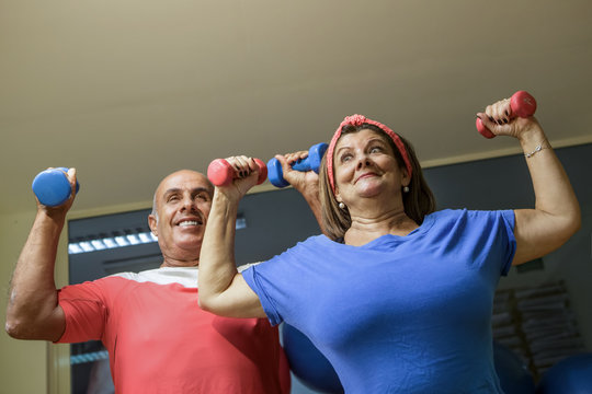 Coppia di anziani felice, lei vestita di blu e lui vestito di rosso si allena felicemente in palestra