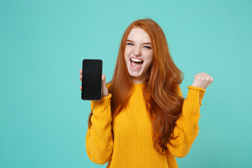 Joyful young redhead girl in yellow sweater posing isolated on blue turquoise background. People...