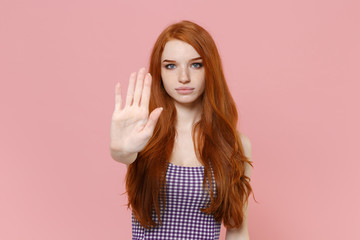 Serious young redhead woman girl in plaid dress posing isolated on pastel pink wall background studio portrait. People emotions lifestyle concept. Mock up copy space. Showing stop gesture with palm.