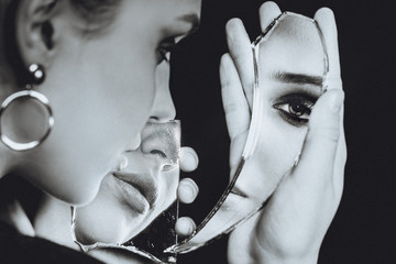 Woman with broken self-image mirror on black background, black and white portrait