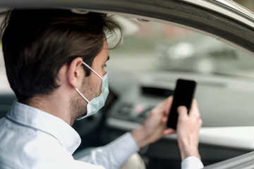 Man with protective mask and having chat on his mobile and traveling in car.