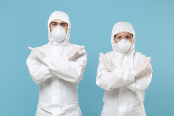 Two people in protective suits respirator masks isolated on blue background studio. Epidemic pandemic new rapidly spreading coronavirus 2019-ncov originating in Wuhan China, virus concept stop gesture