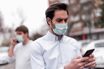 Two businessmen walking outdoor with protective masks and checking them mobiles