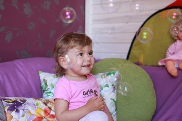 Cute little Caucasian girl one year old plays in her room with soap bubbles, laughs merrily, close-up. Childhood, leisure, games.