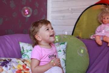 Cute little Caucasian girl one year old plays in her room with soap bubbles, laughs merrily, close-up. Childhood, leisure, games.