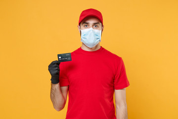 Fototapeta na wymiar Delivery man red cap blank t-shirt uniform mask gloves isolated on yellow background studio Guy employee work courier hold credit card Service quarantine pandemic coronavirus virus 2019-ncov concept.