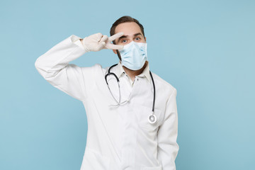 Excited male doctor man in white medical gown sterile face mask gloves isolated on blue wall...