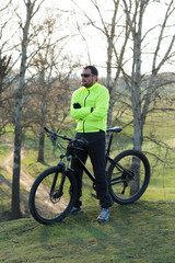 Obraz premium Cyclist in pants and green jacket on a modern carbon hardtail bike with an air suspension fork. The guy on the top of the hill rides a bike.
