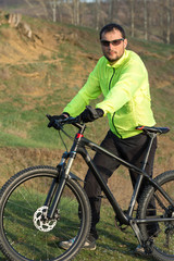 Obraz premium Cyclist in pants and green jacket on a modern carbon hardtail bike with an air suspension fork. The guy on the top of the hill rides a bike.