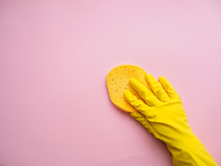 Hand mit Gummihandschuh und gelben Schwamm auf einem rosa Hintergrund, Draufsicht, Frühjahrsputz, Hygiene, Keimfrei