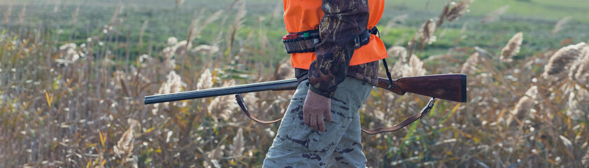 A man with a gun in his hands and an orange vest on a pheasant hunt in a wooded area in cloudy...