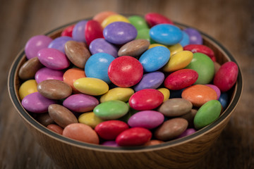 Colorful candies in a wooden bowl case isolated on wood background