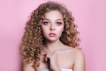 blonde girl with long and shiny curly hair . Beautiful model woman with wavy hairstyle on pink background - obrazy, fototapety, plakaty