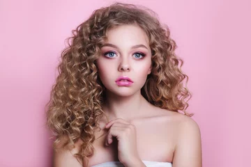 Foto op Plexiglas blonde girl with long and shiny curly hair . Beautiful model woman with wavy hairstyle on pink background © Elena Kratovich
