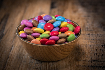 Colorful candies in a wooden bowl case isolated on wood background