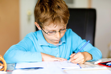 Naklejka na ściany i meble Hard-working happy school kid boy making homework during quarantine time from corona pandemic disease. Healthy child writing with pen, staying at home. Homeschooling concept