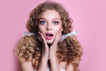 Woman with pink lips and nails surprise holds cheeks by hand on pink background