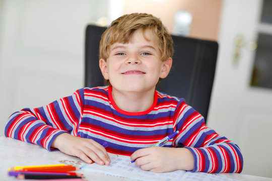 Hard-working happy school kid boy making homework during quarantine time from corona pandemic disease. Healthy child writing with pen, staying at home. Homeschooling concept