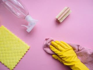 Putzutensilien und eine Hand mit einem gelben Gummihandschuh auf einem rosa Hintergrund, Flat lay,...