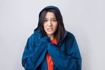 Portrait of a smiling girl dressed in blue raincoat in drops posing with hood on grey background in a studio.