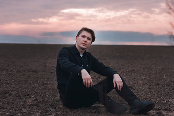  Young man in black in the field. Pink sunset. Serious businessman