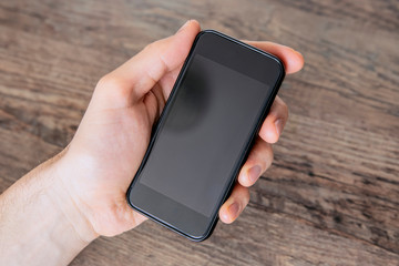 Man holding black blank smartphone with his left hand, close up, neutral background, view from above. Communication concept.