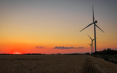 Obraz premium Turbiny wiatrowe i pola uprawne w letni dzień. Produkcja energii, czysta i odnawialna energia.