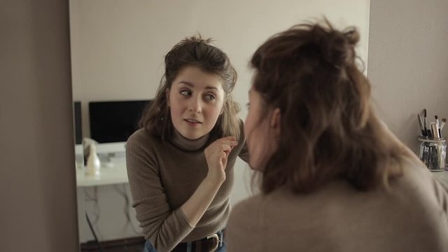 A young girl in front of a mirror examines her hair and pulls out gray hair