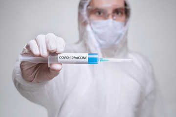 Young scientist in a protective suit and mask holding in his hand injection syringe with vaccine from Coronavirus. COVID-19 outbreak and pandemic infectious concept. Isolated on white background