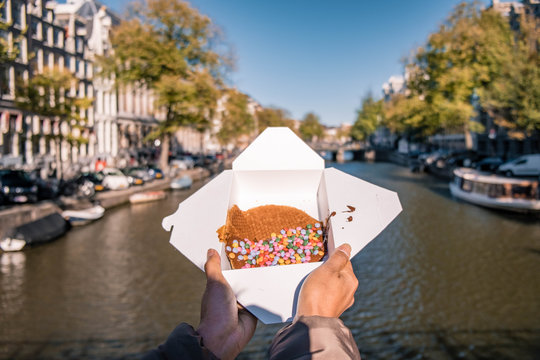 Amsterdam Netherlands, woman hand with Stroopwafel in Amsterdam - typical Dutch food - two circular pieces of waffle filled with caramel-like syrup