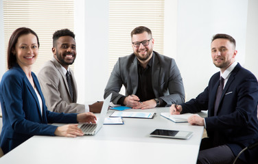 Multy-ethnic group of young business people sitting at the office desk and smiling at camera