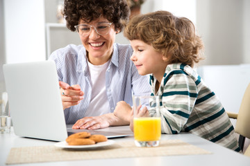 Business woman and her cute little son are using a laptop and smiling while sitting in home office