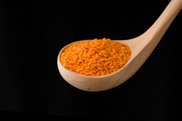 Bright dry orange lentil in a wooden spoon on black background, close up