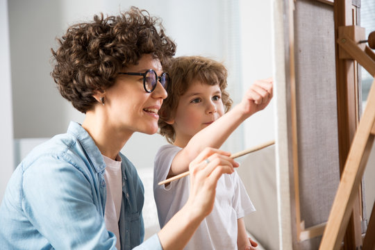 Happy mother and baby son drawing together on a easel