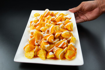 Man's hand holding a plate of chips with two sauces. Rectangular white plate on a black background.Concept of tasty and popular food.