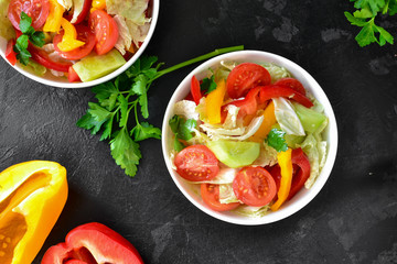 Spring vegetable salad. Salad, tomatoes, cabbage, dressing, bell pepper, cucumber, parsley. Dark background, top view. Healthy vegetarian and vegan food, raw food diet.